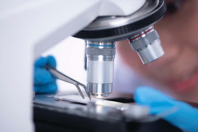 Close up on microscope with scientist holding forceps