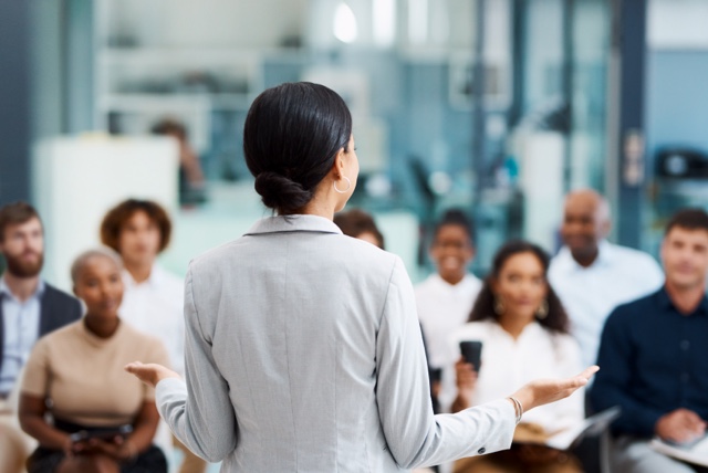 A person standing in front of and talking to an audience